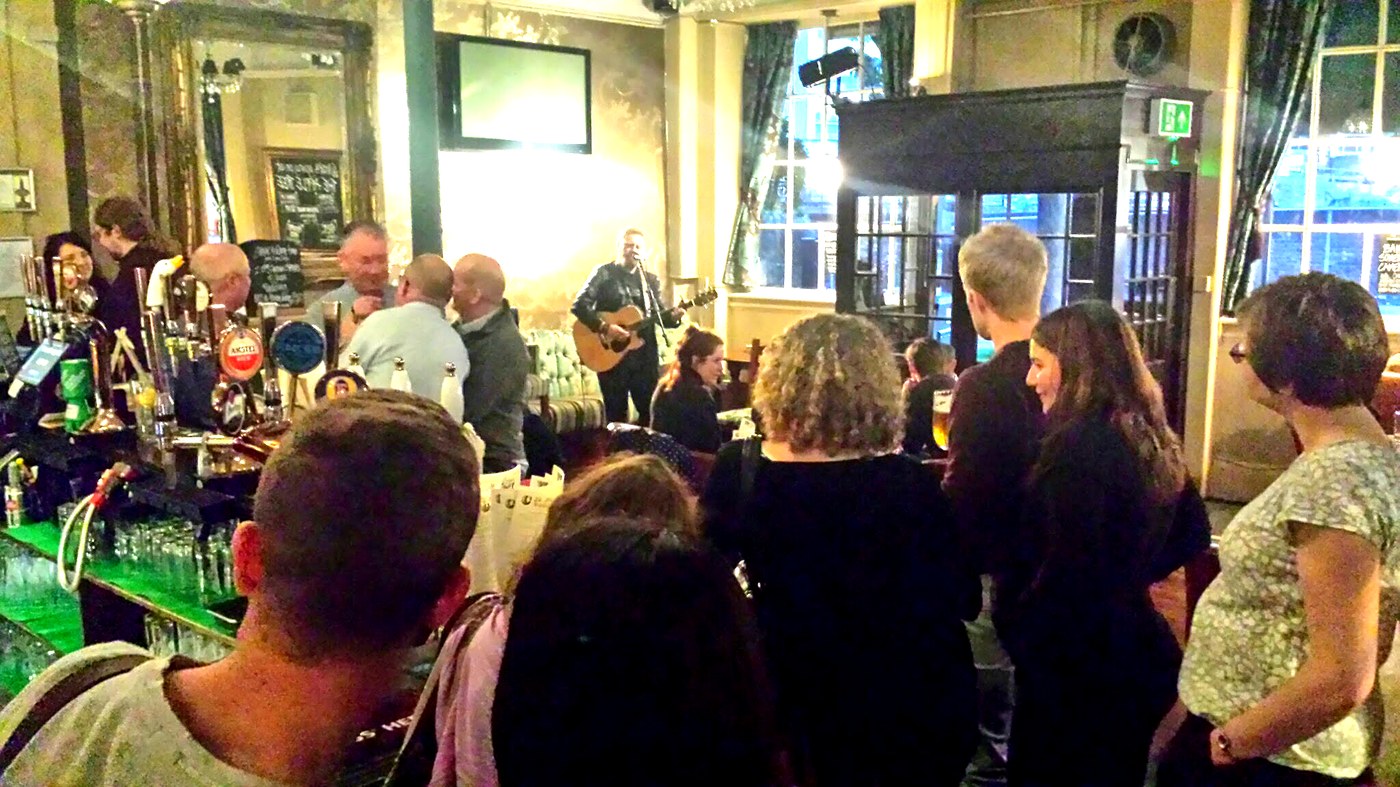 Customers gathered around a live performer in a London pub